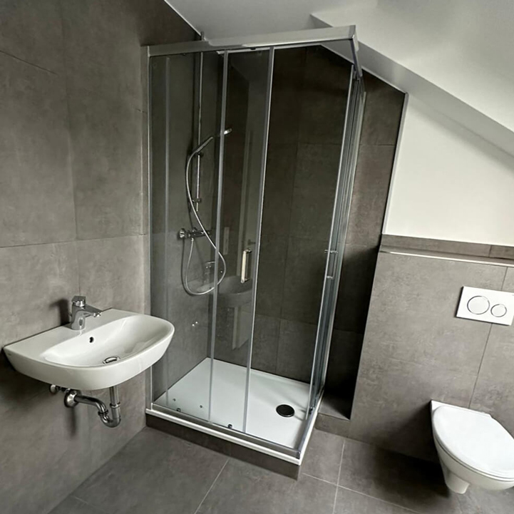 Modernes Gäste-WC mit Dusche, Waschtisch und WC in grauer Fliesenoptik - Professionelle Badsanierung und Installation
